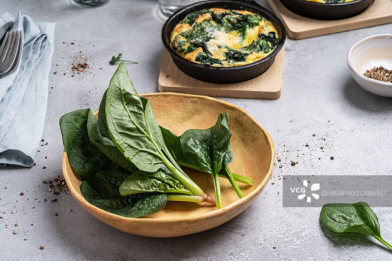 新鲜自家种植的菠菜和铸铁锅中的菠菜煎蛋卷，背景为灰色。图片素材