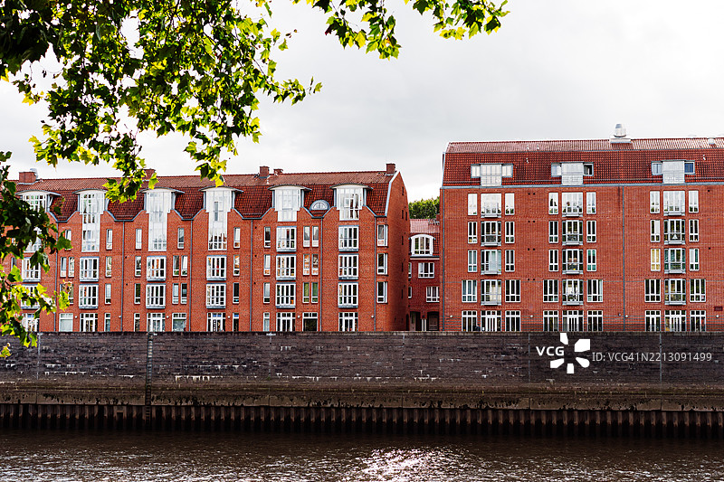 德国不来梅河岸旁现代砖砌住宅建筑，绿树成荫。图片素材