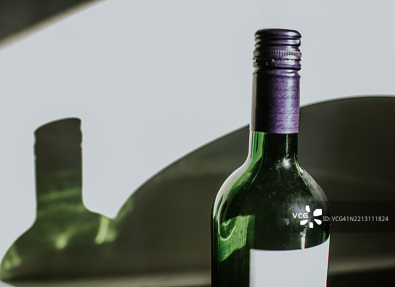 优雅的葡萄酒瓶，紫色瓶盖，置于柔和灯光下的反射面上，营造出温馨的夜晚氛围图片素材