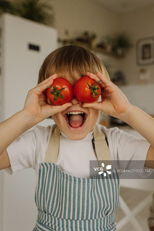 快乐的孩子在有趣的厨房场景中拿着西红柿图片素材