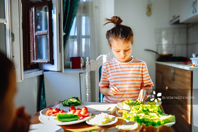 独立的孩子在阳光明媚的家中制作新鲜的蔬菜三明治。图片素材