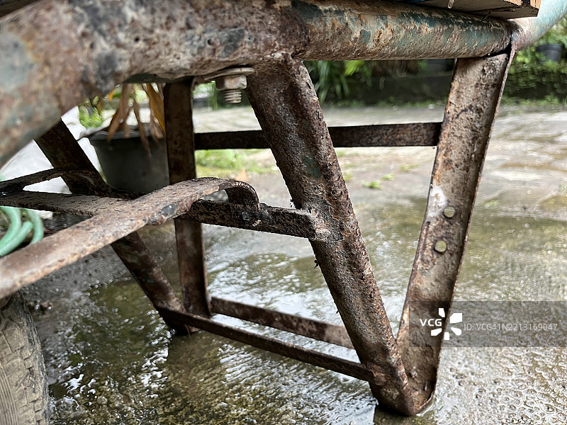 湿润人行道上的生锈手推车框特写图片素材