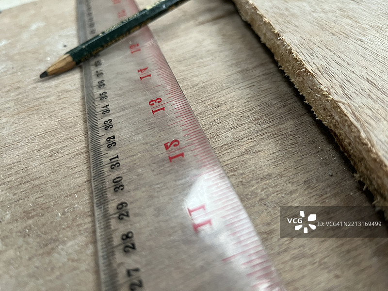胶合板表面上的尺子和铅笔特写，用于木工测量图片素材