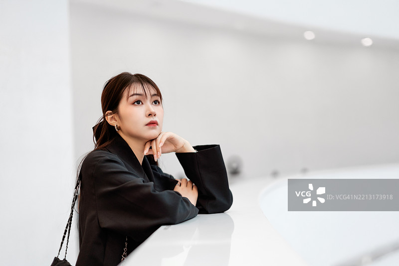 亚洲女性倚靠在现代室内的白色栏杆上。图片素材