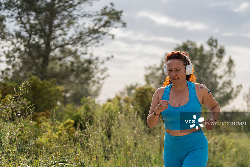 在大自然中慢跑的女性，戴着耳机听音乐图片素材