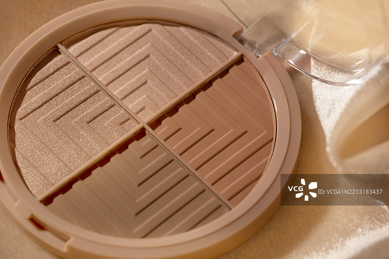 女性化妆品 - 面部粉饼腮红调色板，光泽天鹅绒面料背景上的古铜粉。时尚抽象背景为柔和的米色、粉色和棕色。2025年流行色摩卡慕斯的时尚概念。图片素材