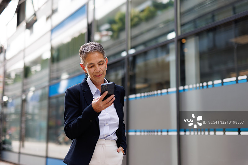 成熟的女商人在办公楼前使用智能手机图片素材