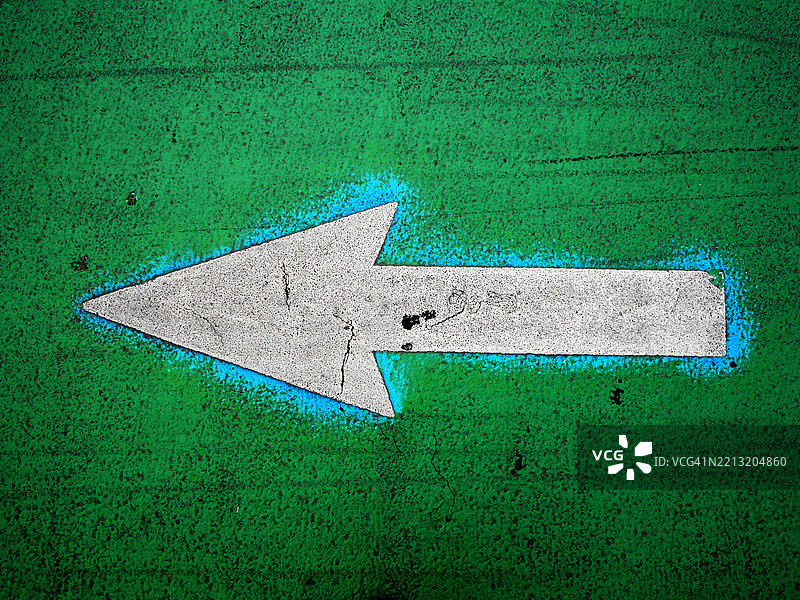 绿色和蓝色背景上的白色箭头。粗糙的纹理。纽约州曼哈顿的道路标记特写。自然的铜绿。光影效果。图片素材