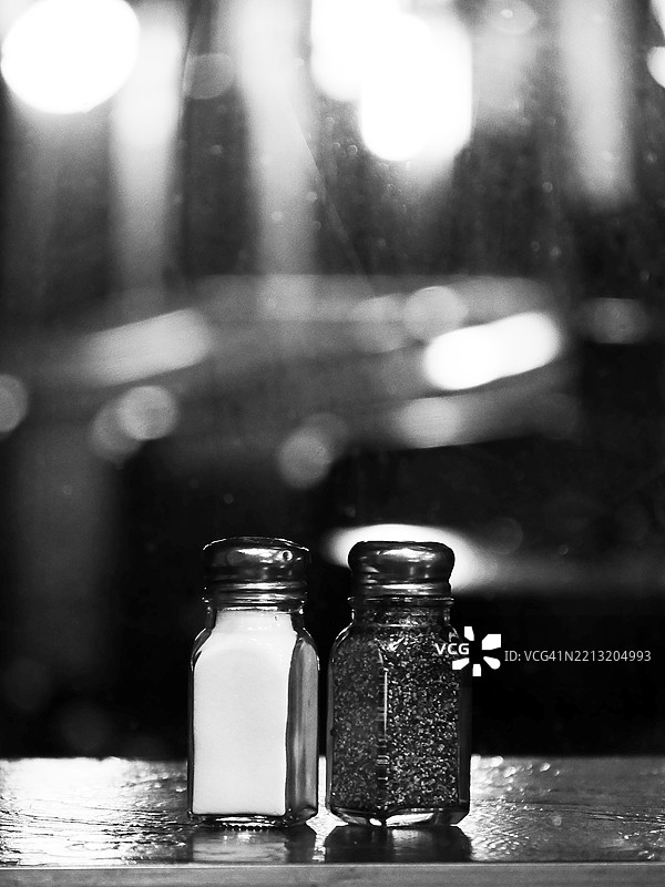 餐厅桌子上的胡椒瓶和盐瓶，背景模糊，自然光，黑白色调，纽约州曼哈顿。图片素材