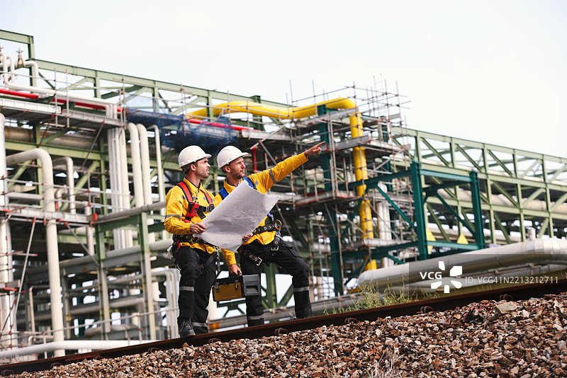 两名穿着安全服和安全帽的工程师在石油管道和管架工业区的背影图片素材