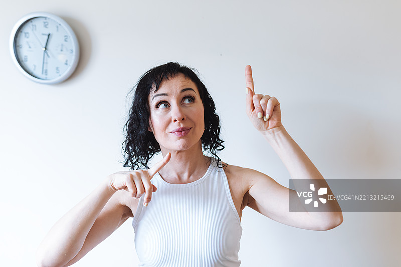 女人在室内指向墙上的时钟，时钟显示着时间图片素材