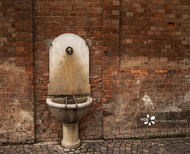 古老的砖墙旁边的古代大理石喷泉。巴罗洛，意大利图片素材