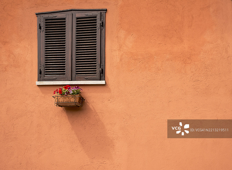 一扇关闭的窗户，明亮的赤土色墙壁和一个投射阴影的小花瓶。图片素材