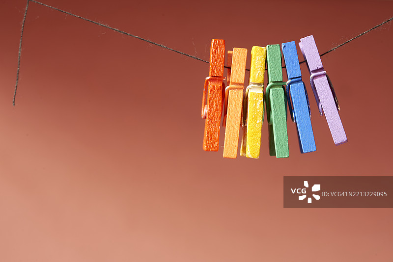 五颜六色的衣夹挂在黑色绳子上，鲜艳的珊瑚色背景形成对比，展现出极简的色彩游戏和奇幻的几何排列。图片素材