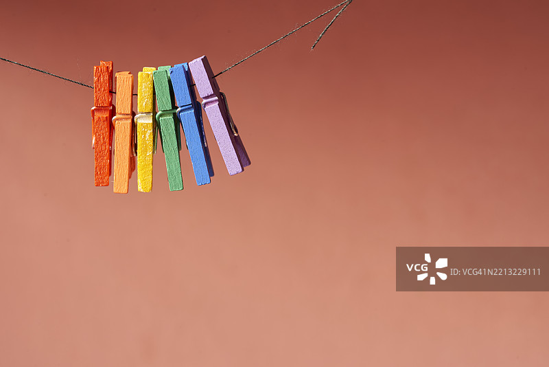 五颜六色的衣夹悬挂在晾衣绳上，背景是明亮的橙色，形成鲜艳的线条，留有干净的空间供图形设计使用。图片素材