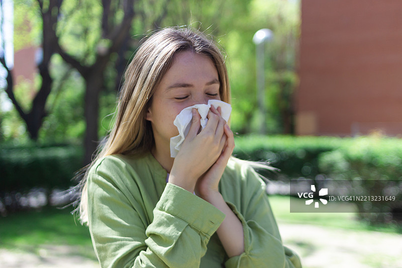 年轻女性在户外擤鼻涕，因季节性过敏而痛苦图片素材