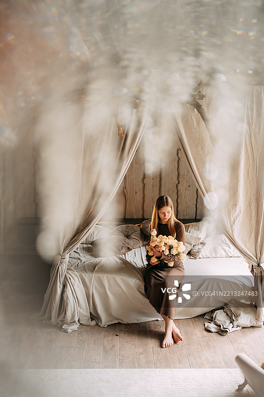 年轻女性坐在舒适的房间里，手里捧着玫瑰花。图片素材