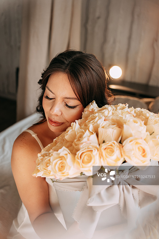 美丽的年轻女性手捧一个装有桃色玫瑰的帽子盒。图片素材