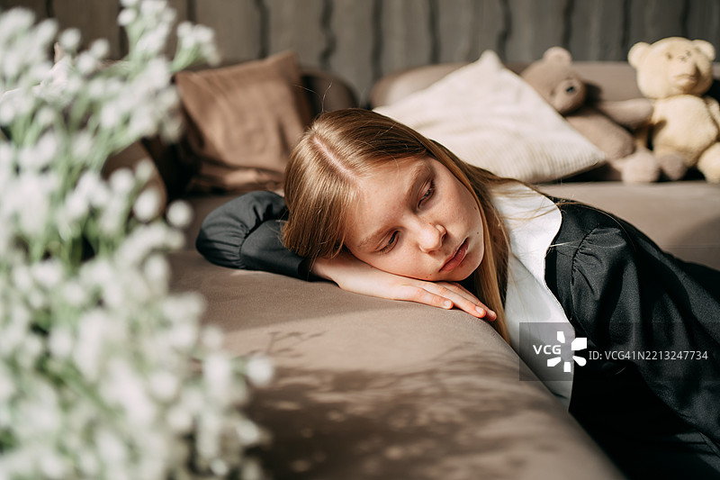伤心的小女孩躺在沙发上，身边有毛绒玩具熊。图片素材