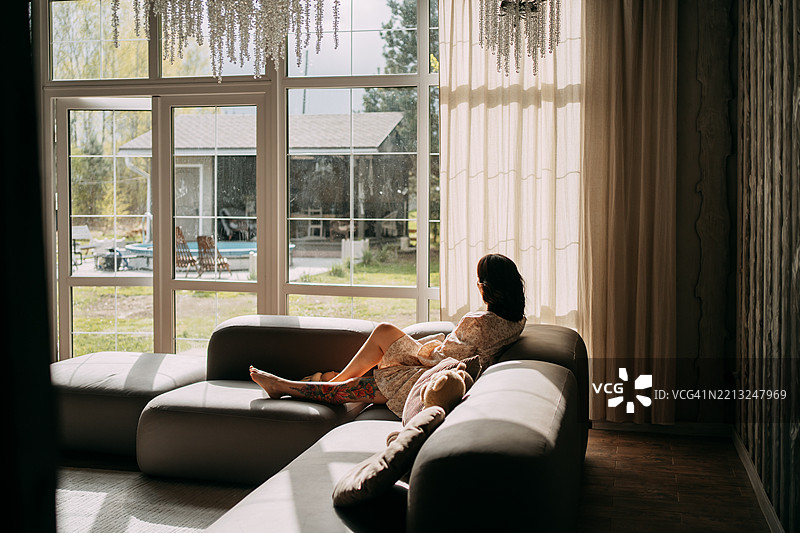 年轻女性在沙发上放松，望着家中的窗外。图片素材