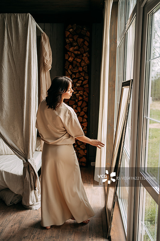 年轻女性在乡村风格的卧室里照镜子。图片素材