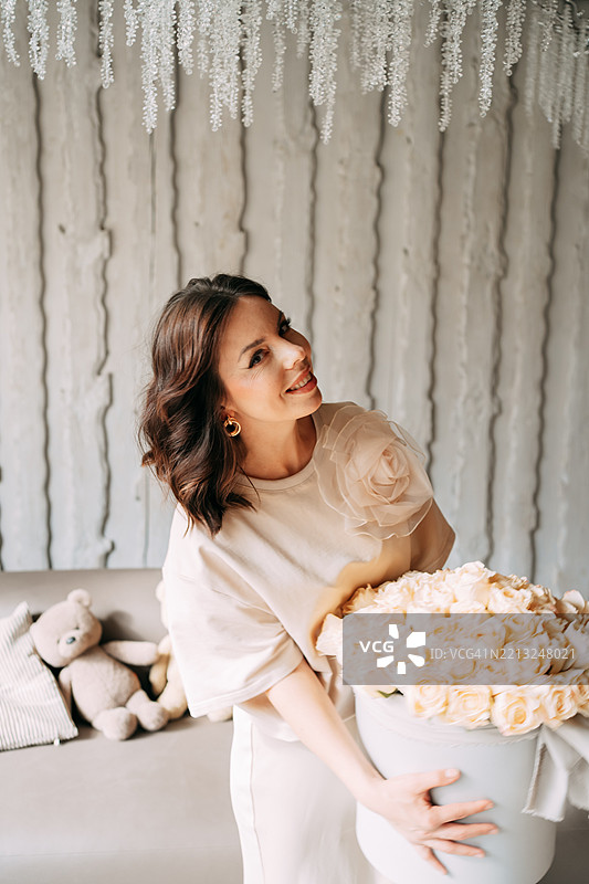 快乐的女人在时尚的室内抱着一大盒白玫瑰图片素材