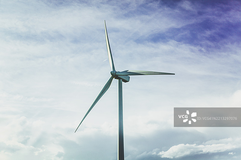 一座大型风力涡轮机高耸在晴朗的蓝天背景下，正在乡村捕捉可再生能源。图片素材