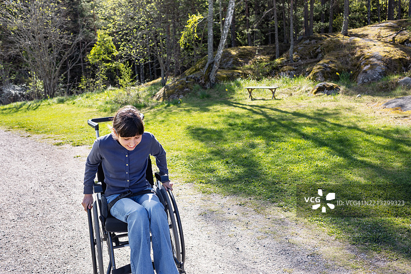 在宁静的林地中移动的神经多样性青少年女孩坐在轮椅上图片素材