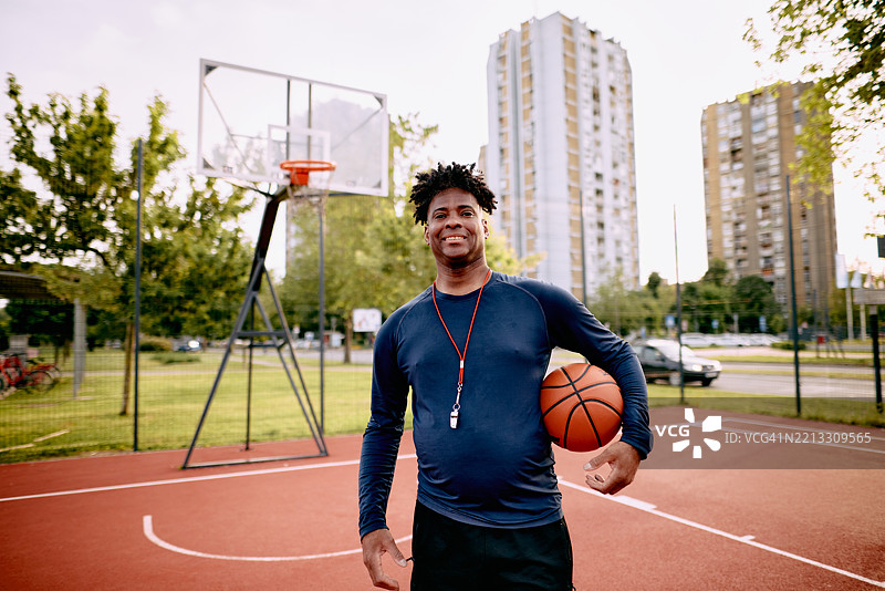 微笑的篮球教练在户外球场上握着篮球图片素材