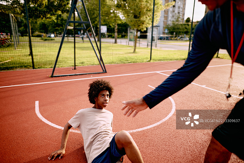 教练帮助年轻篮球运动员在球场上站起来图片素材