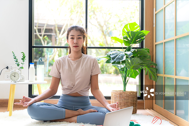 生活方式女性瑜伽锻炼与姿势，追求健康生活。年轻人们在客厅在线进行平衡身体、活力、禅修和冥想的锻炼与健身运动。图片素材