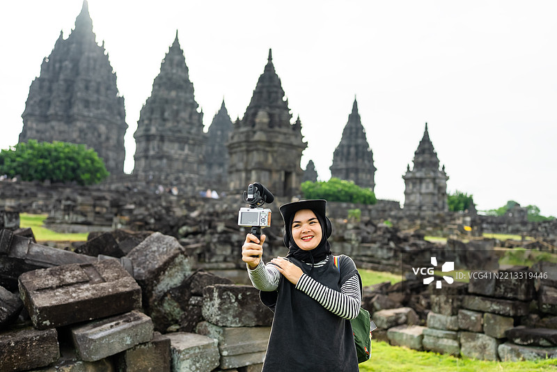 迷人的穆斯林女性在录制视频博客，一位游客在普兰巴南寺记录她的旅行经历，捕捉美好回忆。图片素材