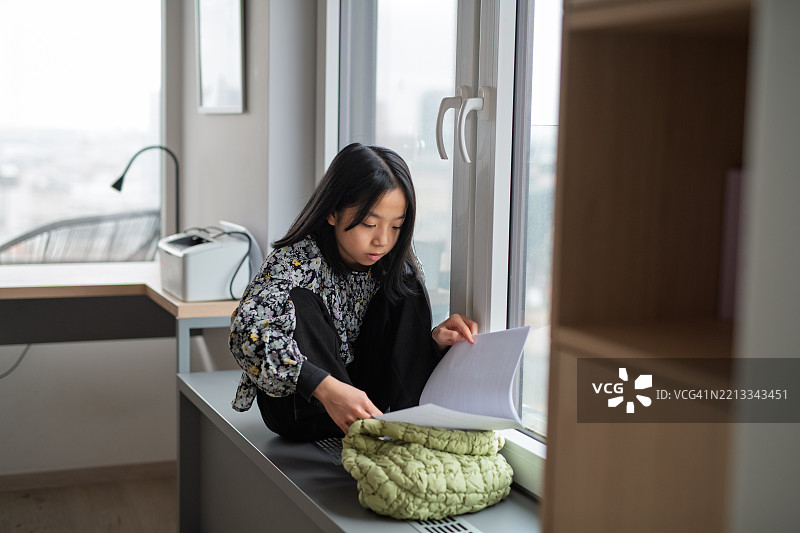 年轻女孩坐在窗边在家里使用智能手机图片素材