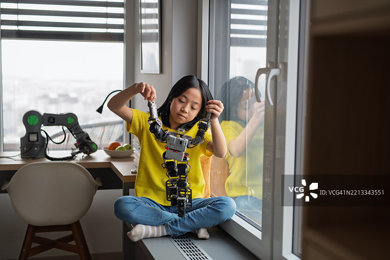 好奇的女孩在家里与类人机器人玩耍。图片素材