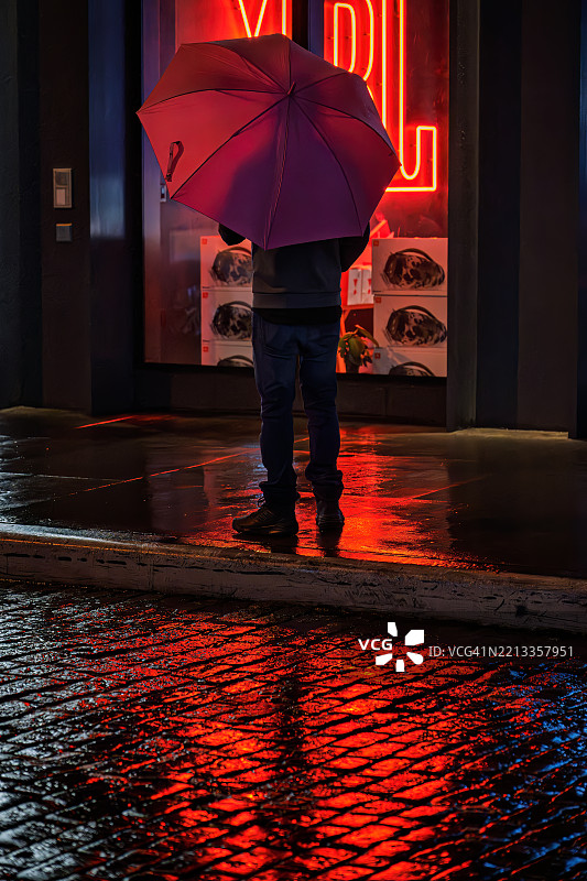 年轻男子背影的剪影,手持红色雨伞,雨夜中在曼哈顿休斯顿街的红色倒影图片素材