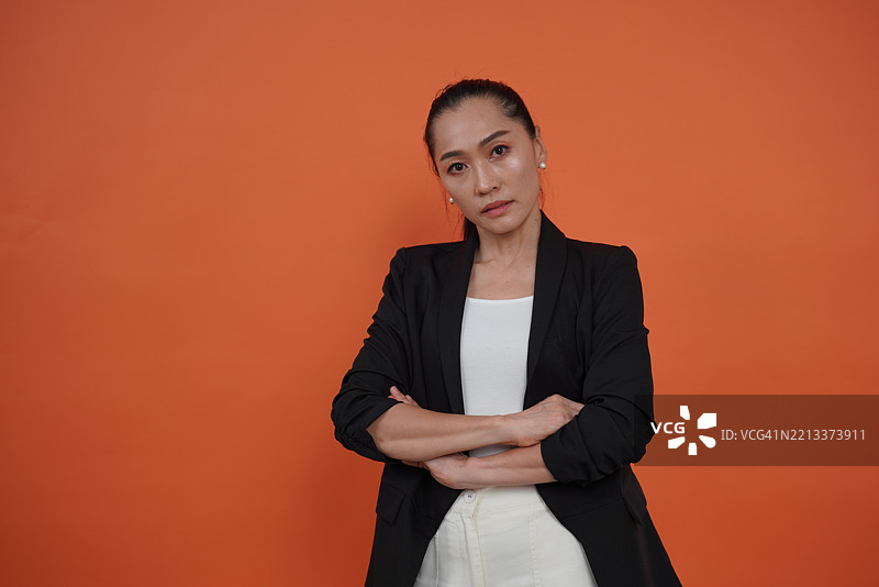 穿着黑色西装外套的女性，站在橙色背景前。图片素材