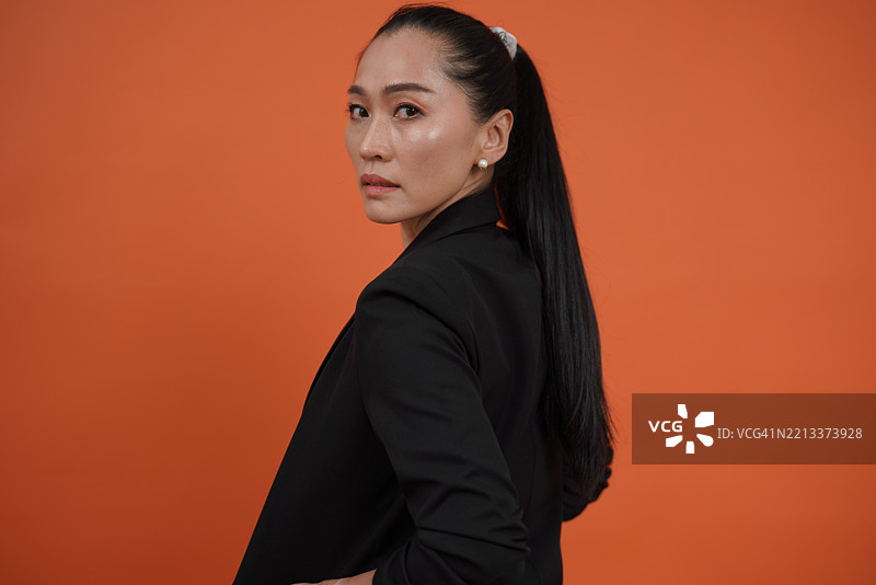 穿着黑色西装外套的女性，站在橙色背景前。图片素材