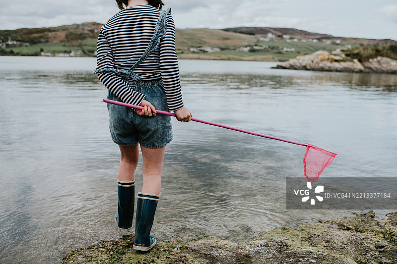 孩子在阴天的海岸风景附近用网探索浅水区图片素材