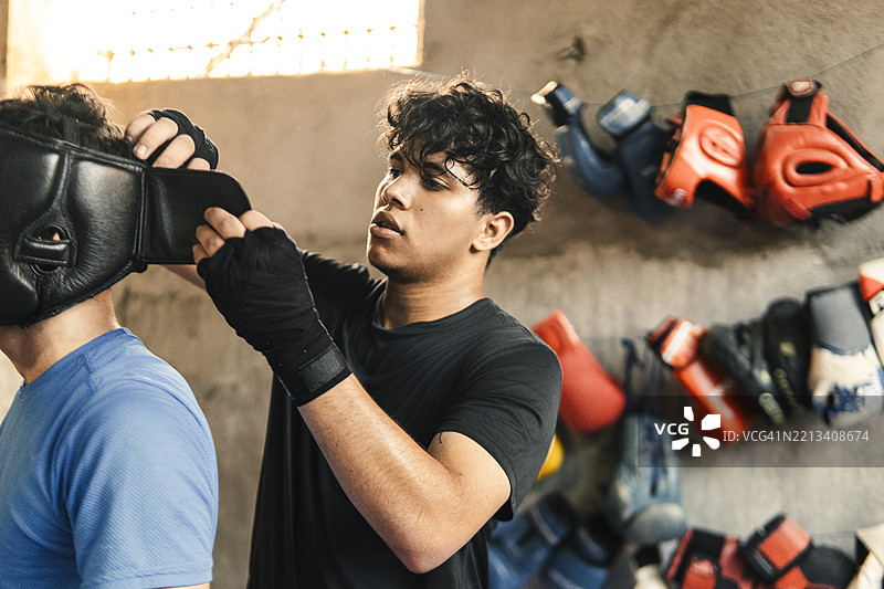 年轻拳击手在拳击馆里帮助佩戴头盔的训练伙伴。图片素材