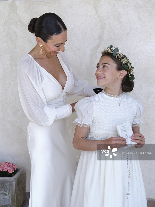 母亲在女儿的第一次圣餐仪式前为她整理裙子图片素材