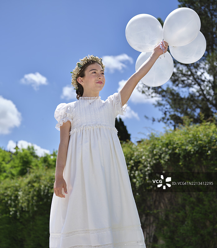 穿着第一次圣餐礼服的女孩手持白色气球图片素材