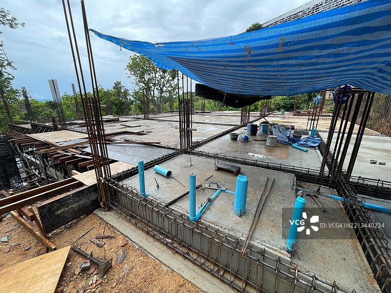 一个建筑工地，展示了新浇筑的混凝土板，上面有蓝色的管道、竖直的钢筋，以及遮阳的防水布。图片素材