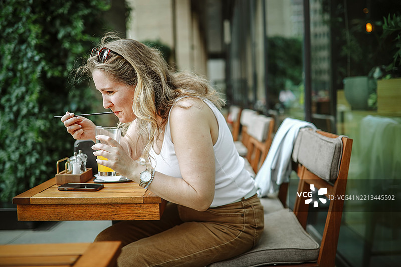 女人在城市街头咖啡馆享用无酒精的新鲜橙子鸡尾酒图片素材