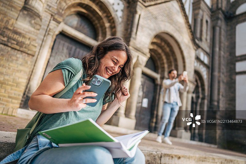 快乐的学生在大学外学习时收到好消息，正在查看智能手机。图片素材