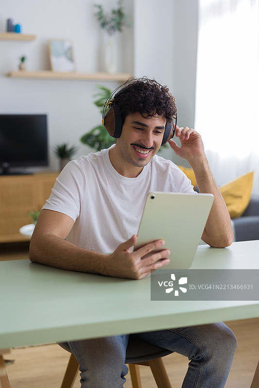 年轻男子在家中享受音乐和视频，使用平板电脑。图片素材
