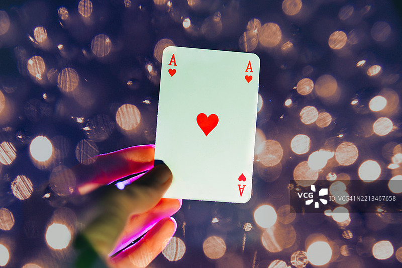 手中拿着黑暗背景上的一张王牌，背景有柔和的散景光点。图片素材