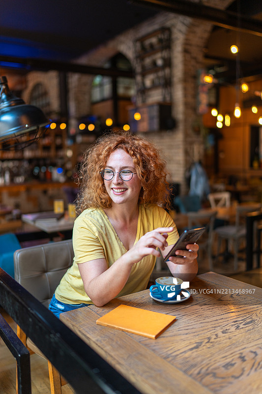 微笑的年轻女性在咖啡馆使用手机图片素材