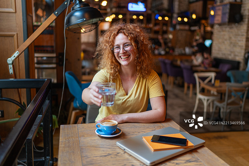 快乐的自由职业者在咖啡馆举杯祝酒，手中是水。图片素材