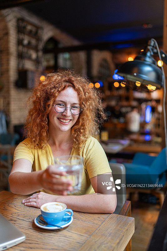 微笑的年轻女性在咖啡馆里递水杯图片素材