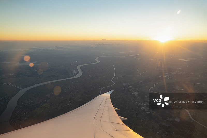 从飞机窗户拍摄的关东平原鸟瞰图，夕阳下富士山在地平线上。图片素材